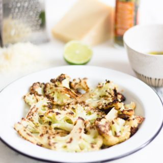 Roasted cauliflower in a bowl with ingredients behind