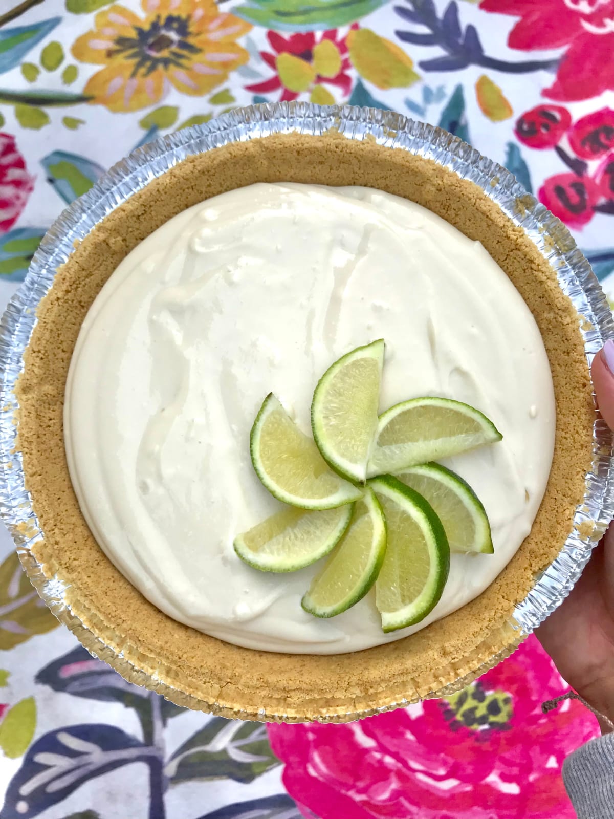 Homemade key lime pie with limes on tip sitting on a pretty floral table cloth