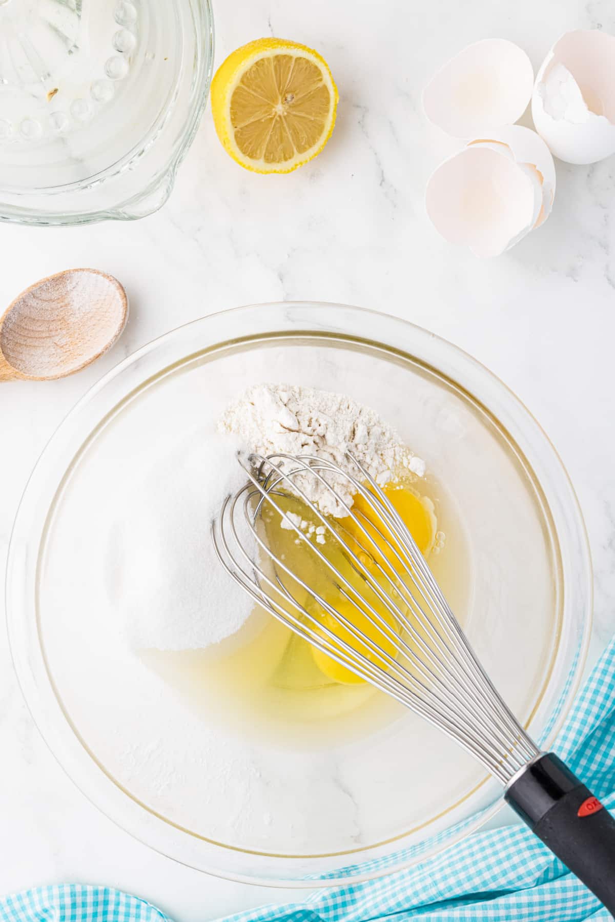 mixing flour, sugar and eggs with a whisk in a clear bowl on a white countertop