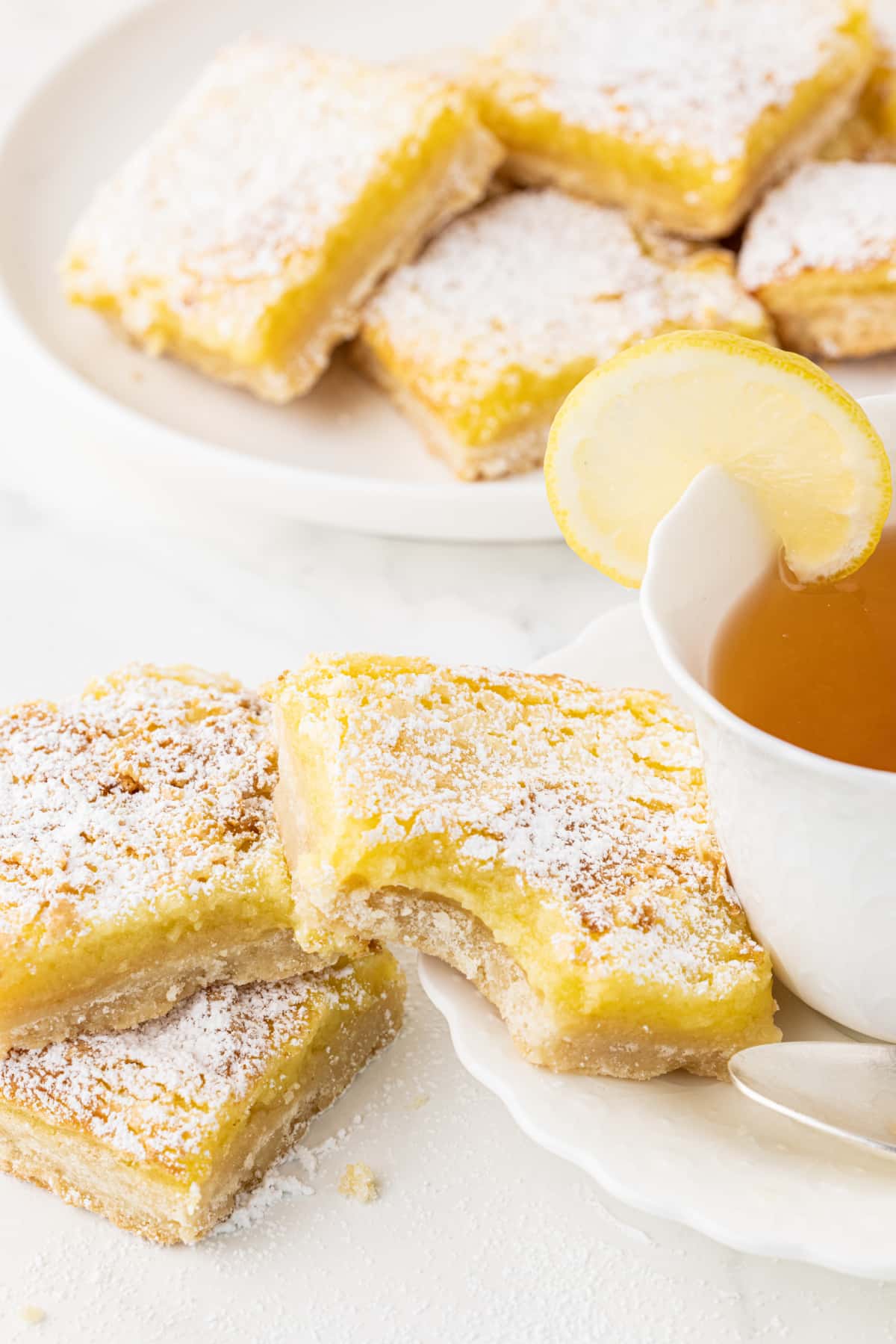 lemon bar cookies with white plates and a tea cup full of tea