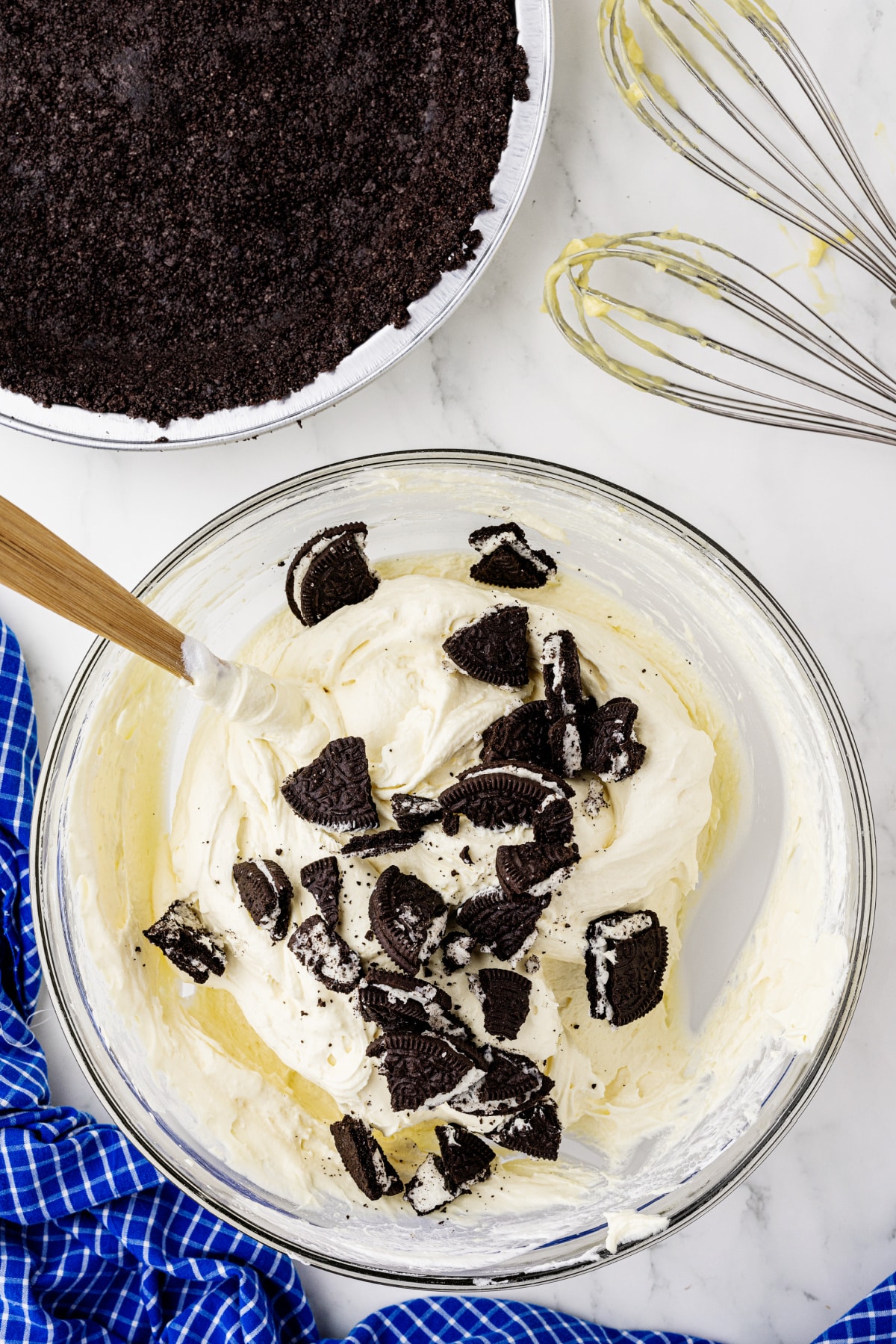 folding crumbled Oreo cookies into a pie filling on a white counter
