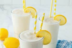 glasses of frosted lemonade on a white counter with a blue dish towel and sliced lemons