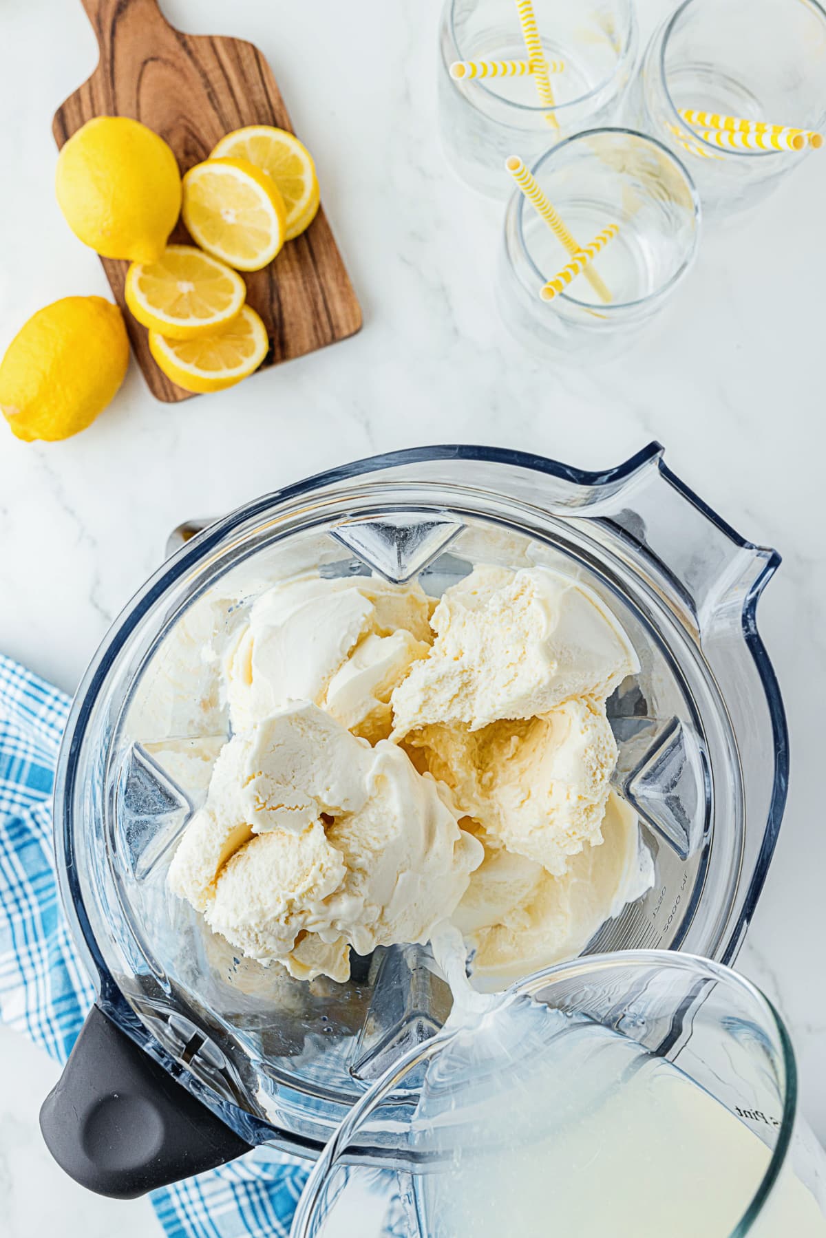 milk pouring into blender full of ice cream with lemons on the cutting board beside it