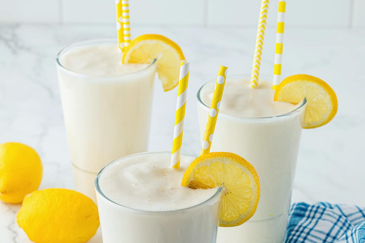 three glasses full of frosted lemonade and topped with lemon wedges