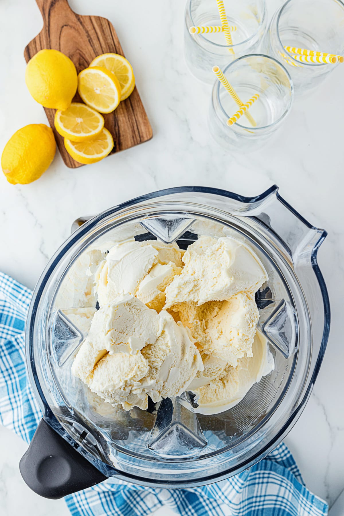 Blender with ice cream in it on a counter with lemons and empty glasses