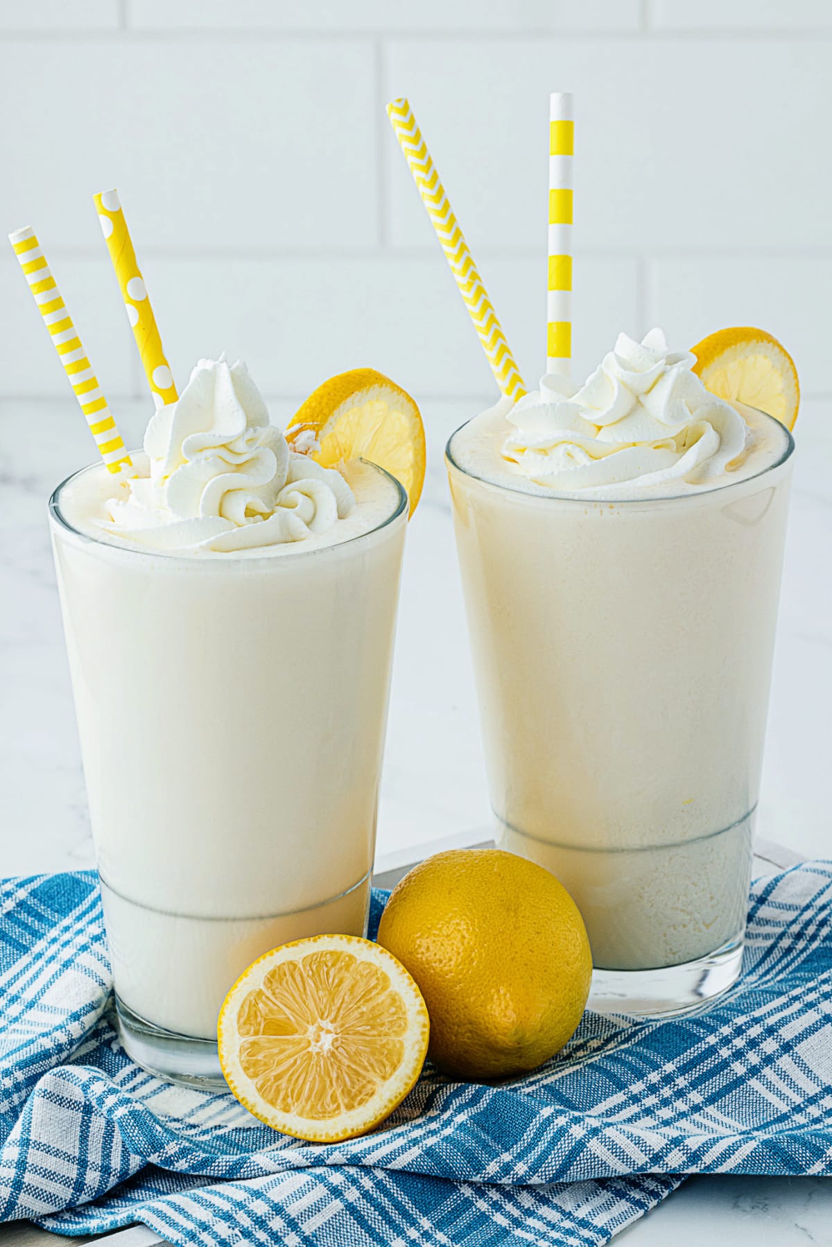 two lemon milkshakes with yellow straws and whipped topping and sliced lemon 