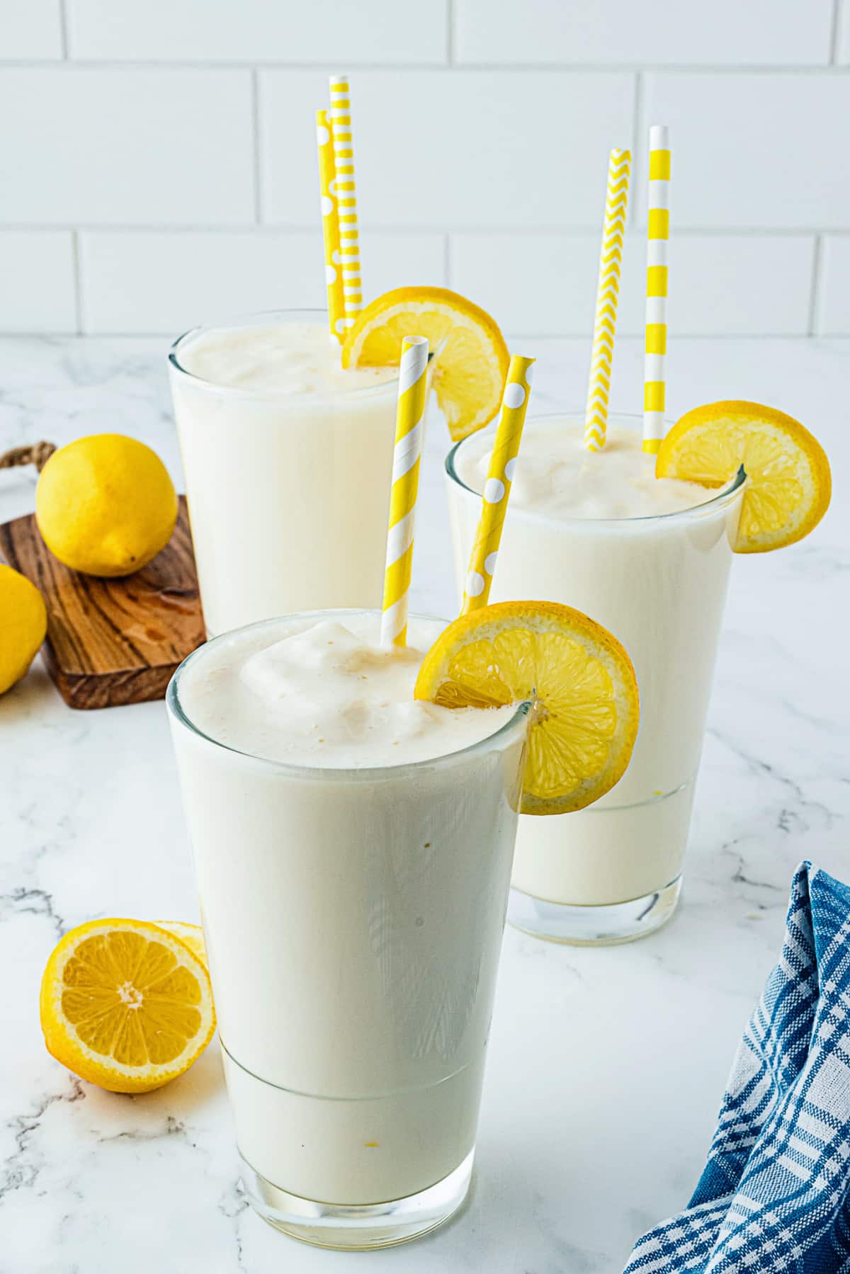 three tall clear glasses full of lemon milkshakes and topped with lemon wedges