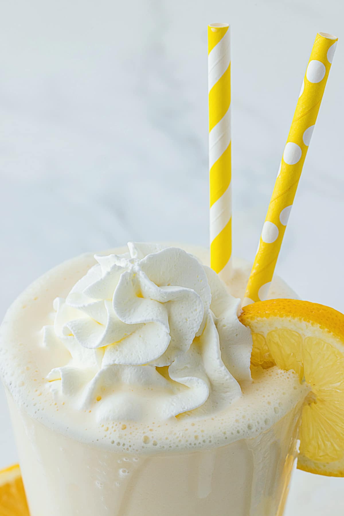 the top of a lemon milkshake with two yellow straws and a lemon wedge