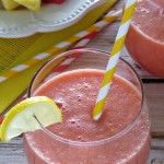 clear glass of watermelon juice with a yellow and white striped straw and lemon wedge