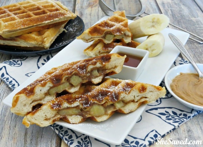 Waffles stuffed with peanut butter and bananas sitting on a serving plate with a cup of syrup topping
