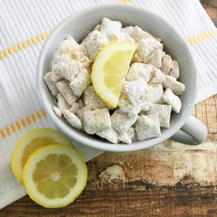 bowl of puppy chow chex mix with lemons on top sitting on a white and yellow napkin