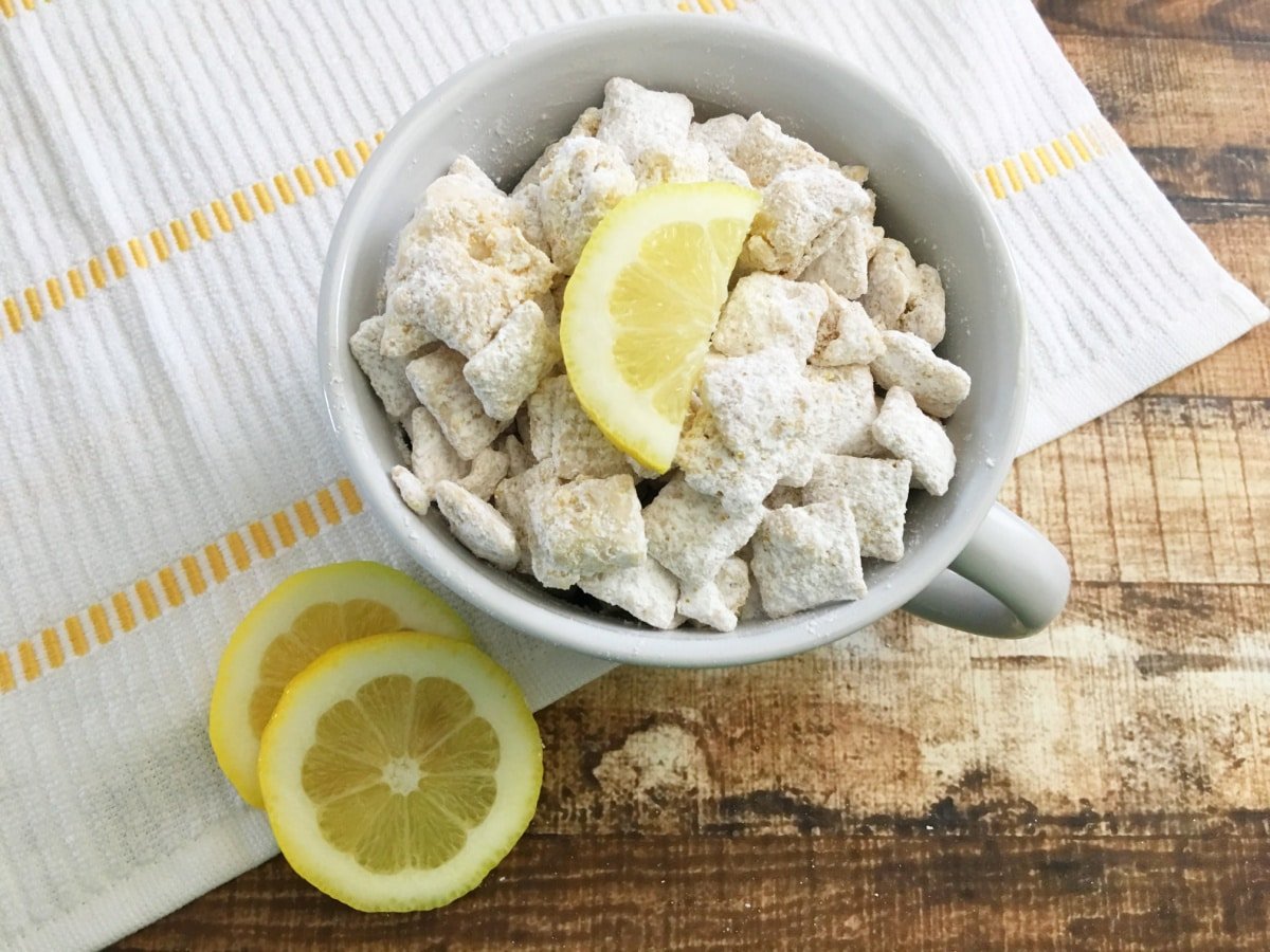 bowl of puppy chow chex mix with lemons on top sitting on a white and yellow napkin