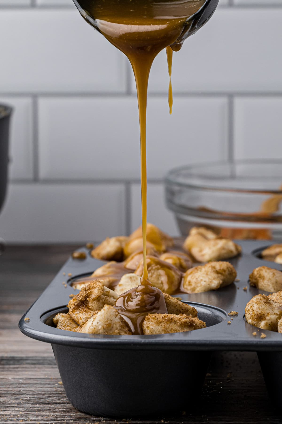 Caramel sauce pouring over bread dough in a muffin tin