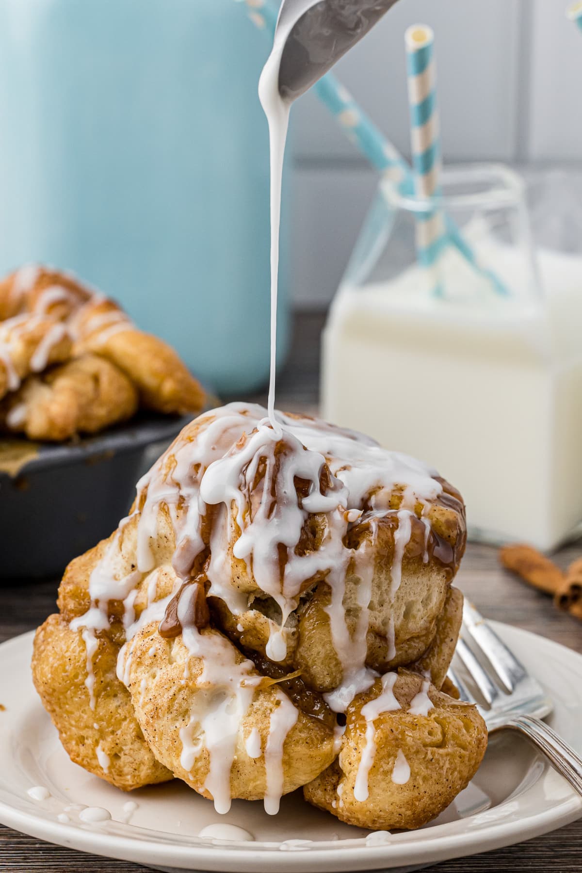icing being drizzled over a cinnamon roll with milk in the background