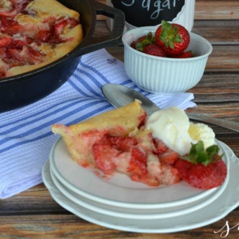 skillet strawberry cobbler on a white plate on a wooden table with a blue and white tablecloth