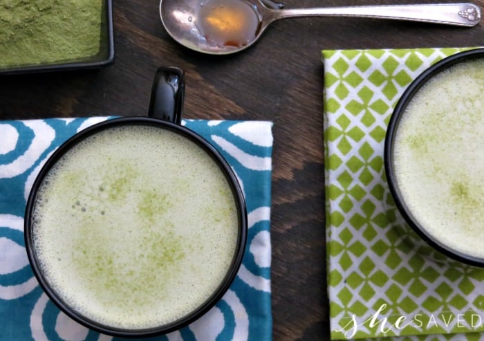 Two cups of Matcha Green Tea Lattes on colorful linens with a teaspoon of honey