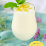 festive glass full of a pineapple shake topped with green mint leaves and pineapple bits