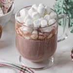 clear glass mug full of hot chocolate topped with mini marshmallows on a Christmas table setting