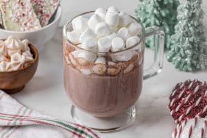 clear glass mug full of hot chocolate topped with mini marshmallows on a Christmas table setting