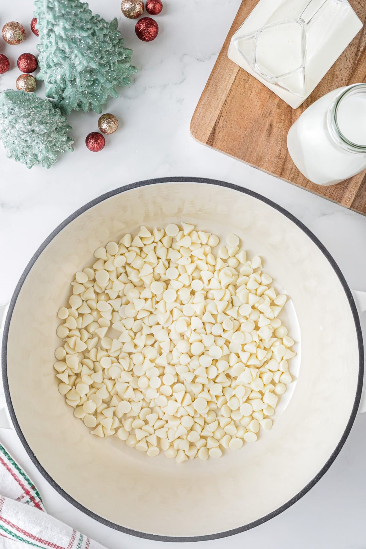 Big bowl of white chocolate chips on a white counter with holiday decor in the background