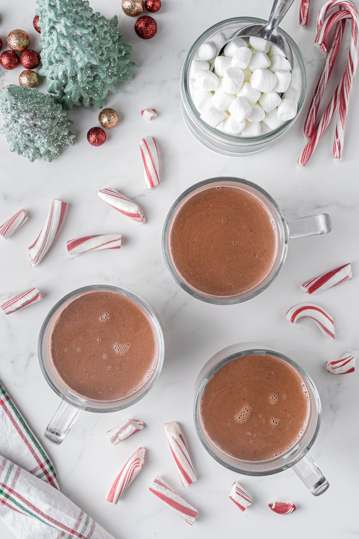 cups of hot chocolate sitting on a counter with candy cane pieces and a mug full of marshmallows