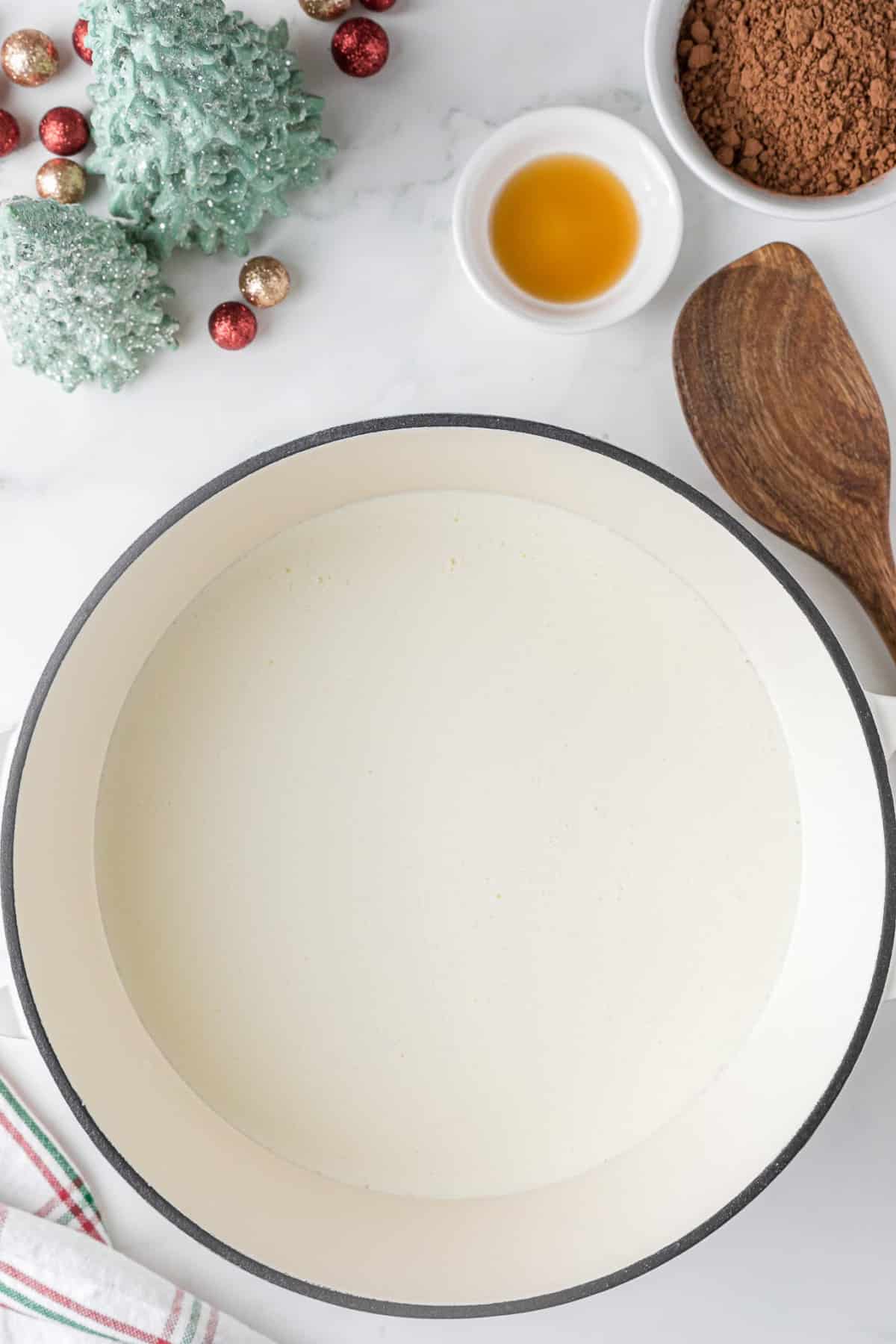 melted white chocolate in a large saucepan on a white counter with a wooden spoon and Christmas decor