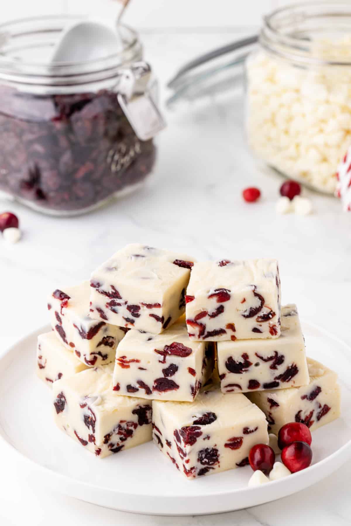white fudge with cranberries on a white plate with dried cranberries and white chocolate chips in the background