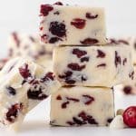 small stack of white fudge with cranberries on a countertop with red berries