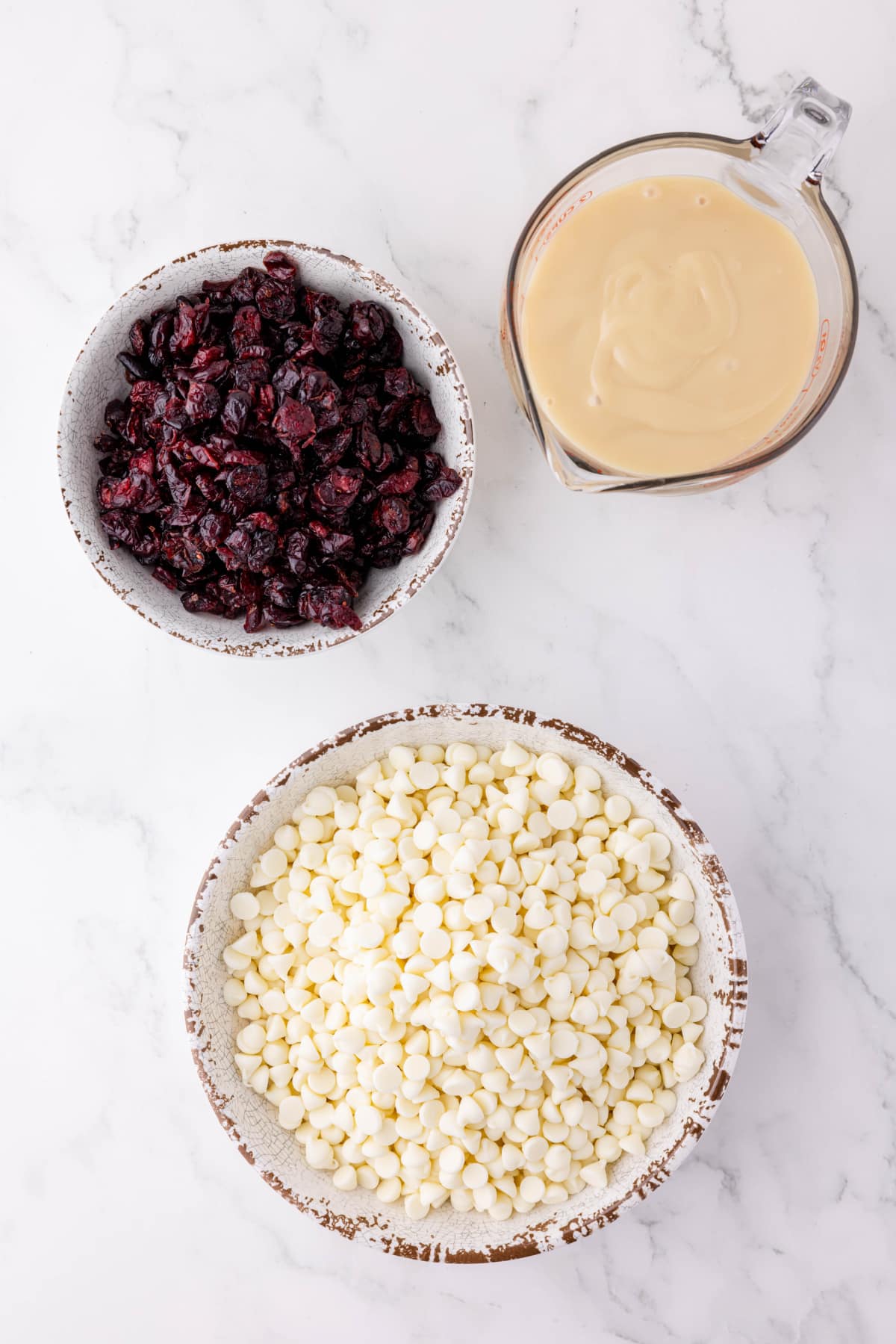 A bowl of white chocolate chips, dried cranberries and sweetened condensed milk sitting on a counter