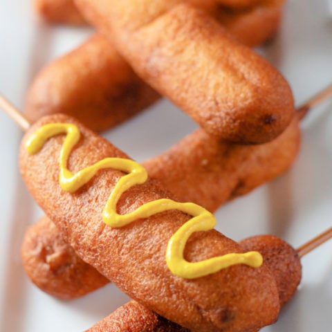 corndogs piled on a plate with mustard drizzled on them