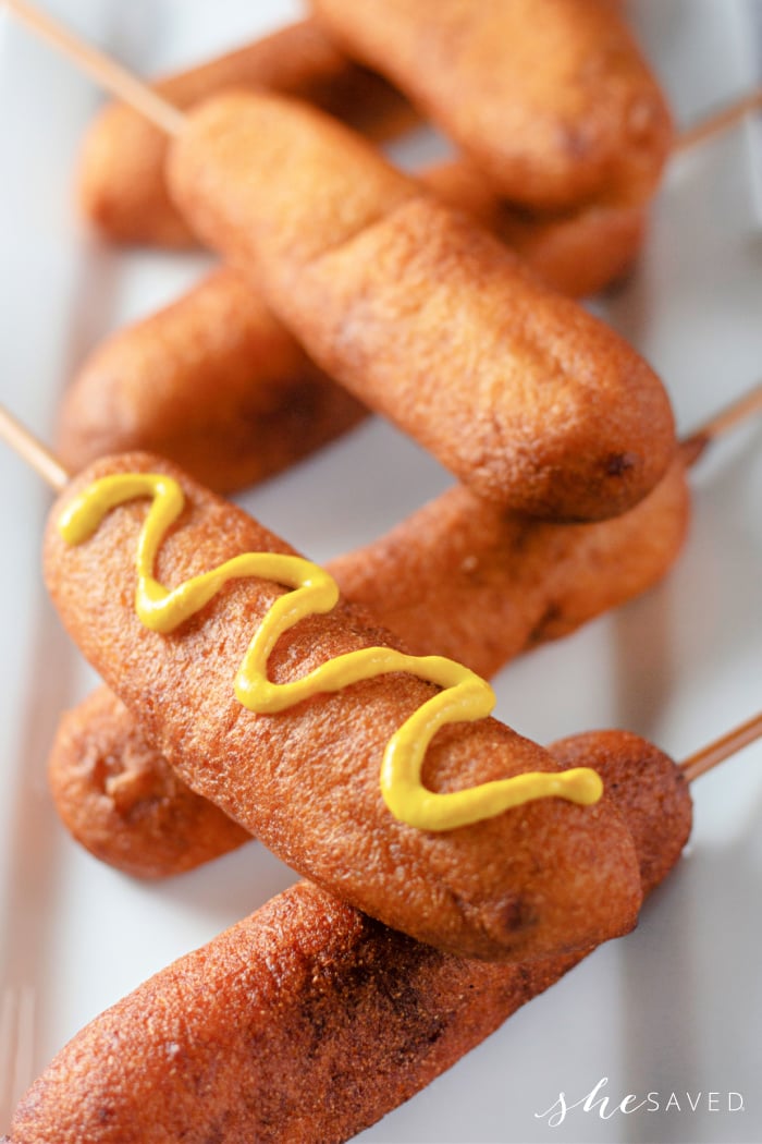 corndogs piled on a plate with mustard drizzled on them