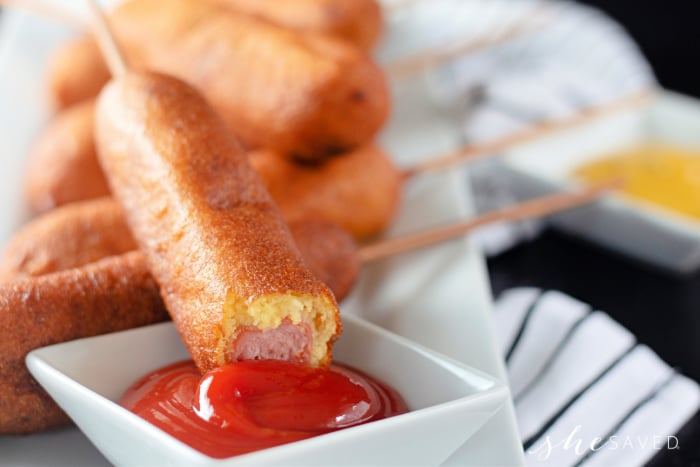 corn dog dipping in red ketchup with a bite out of it