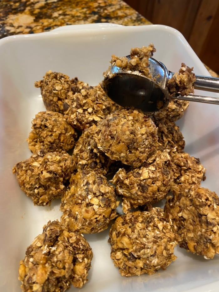 no bake peanut butter bites in a white dish being scooped with an ice cream scooper