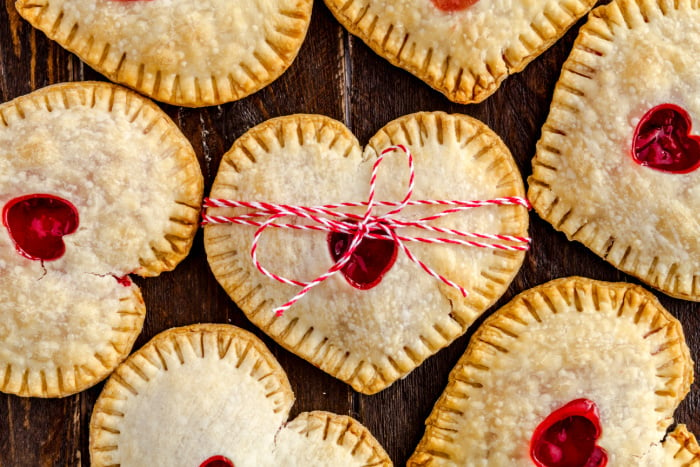 Heart shaped strawberry hand pies on wooden table tied with red and white bakers twine