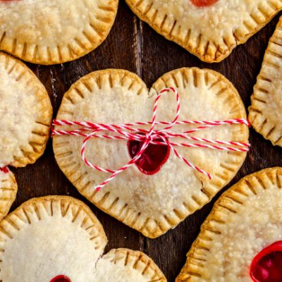 Heart shaped cherry hand pies on wooden table tied with red and white bakers twine