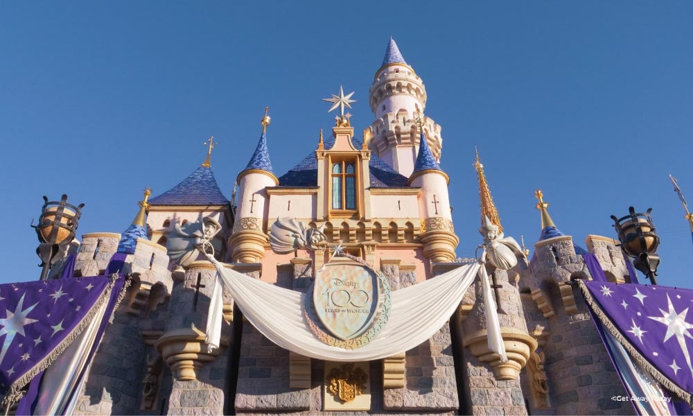 Disneyland Castle adorned with a Disney100 banner with blue sky in the background