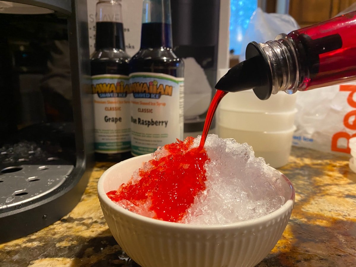 red snow cone syrup being poured onto shaved ice