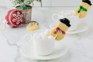 snowman cookies sitting on top of white hot chocolate mugs