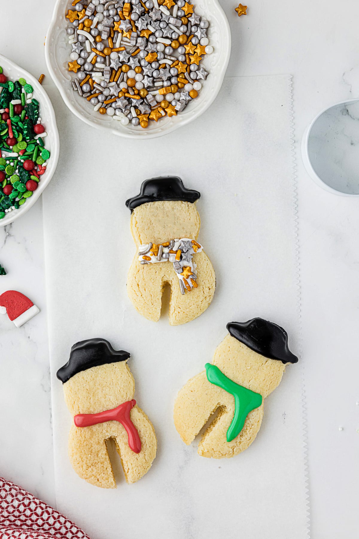 three snowman sugar cookies on counter with sprinkles and frosting