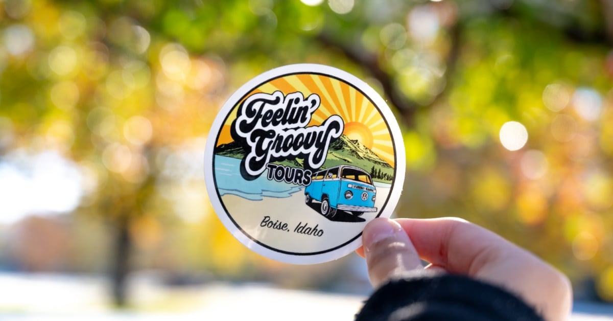 Hand holding up a Feeling Groovy sticker with fall leaves in the background