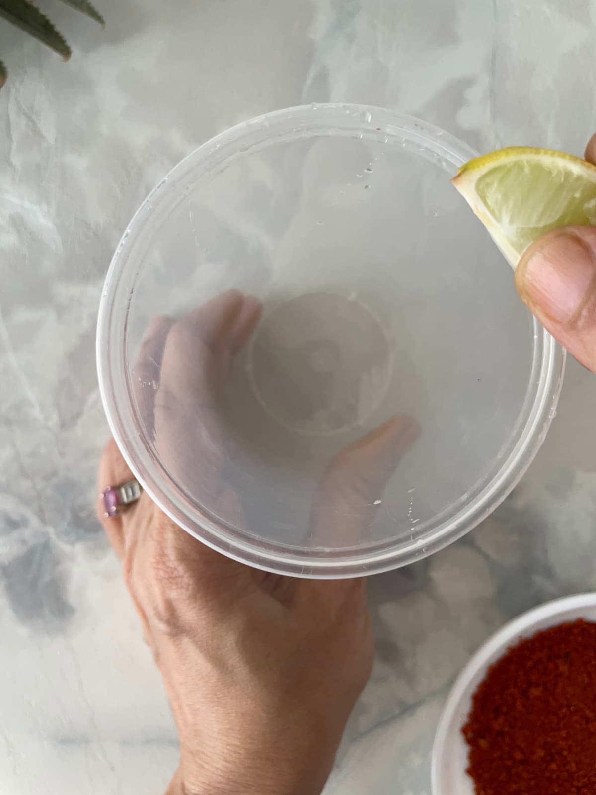 A yellow lime wedge being used to wet the rim of a plastic cup
