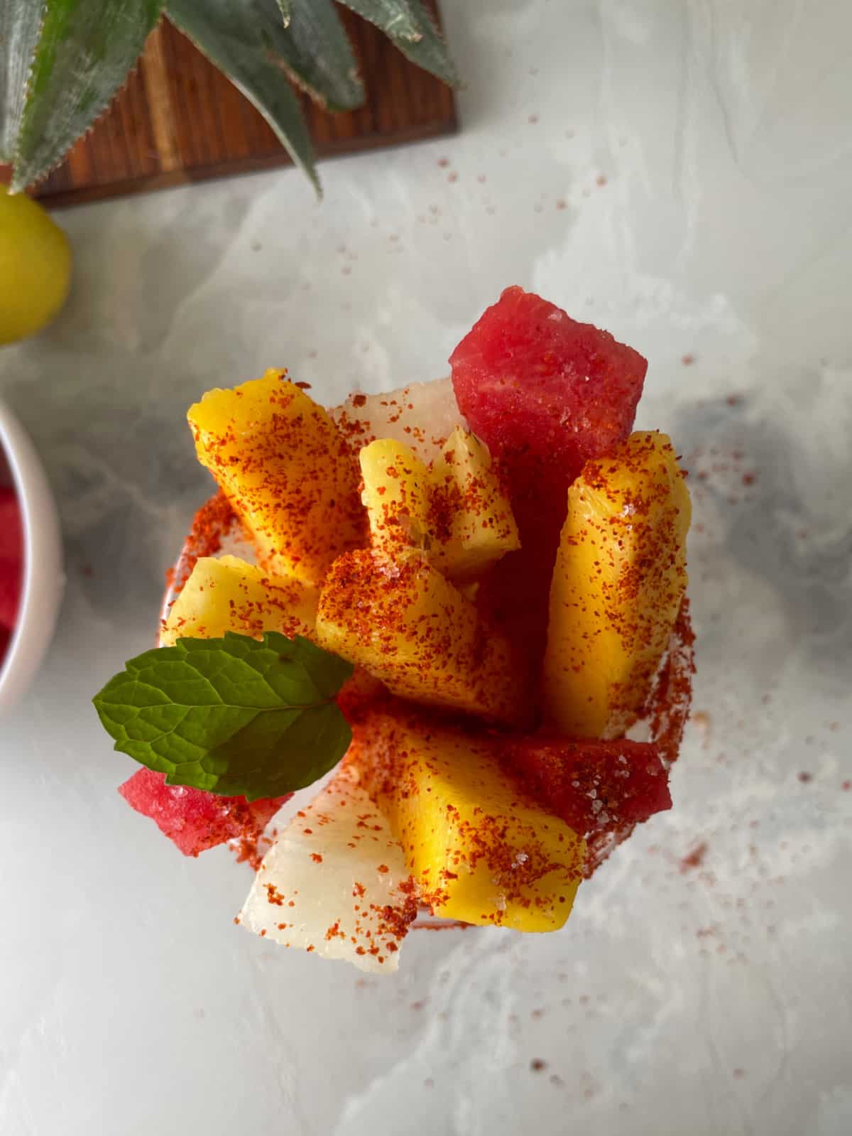 A cup full of fruit spears sprinkled with chili seasoning and a mint leaf