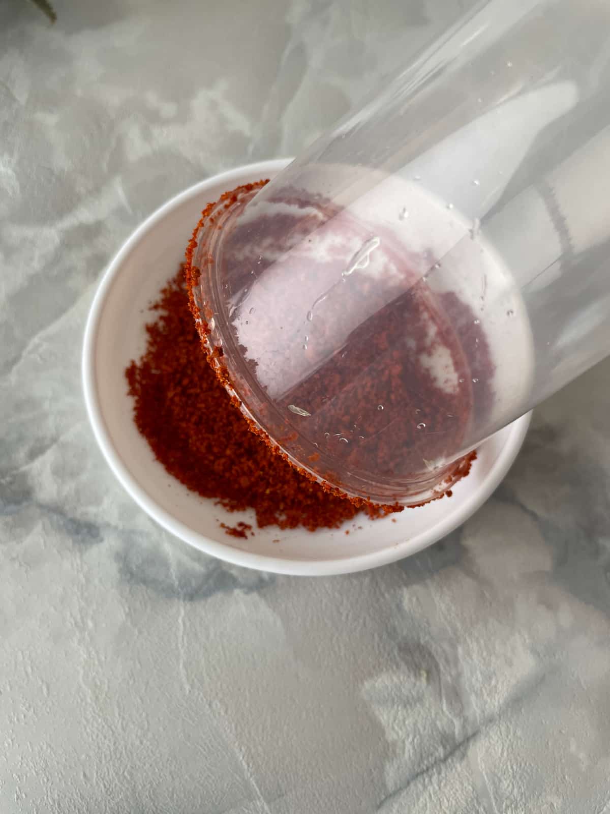 Rim of plastic clear cup being dipped in Tajin spice seasoning