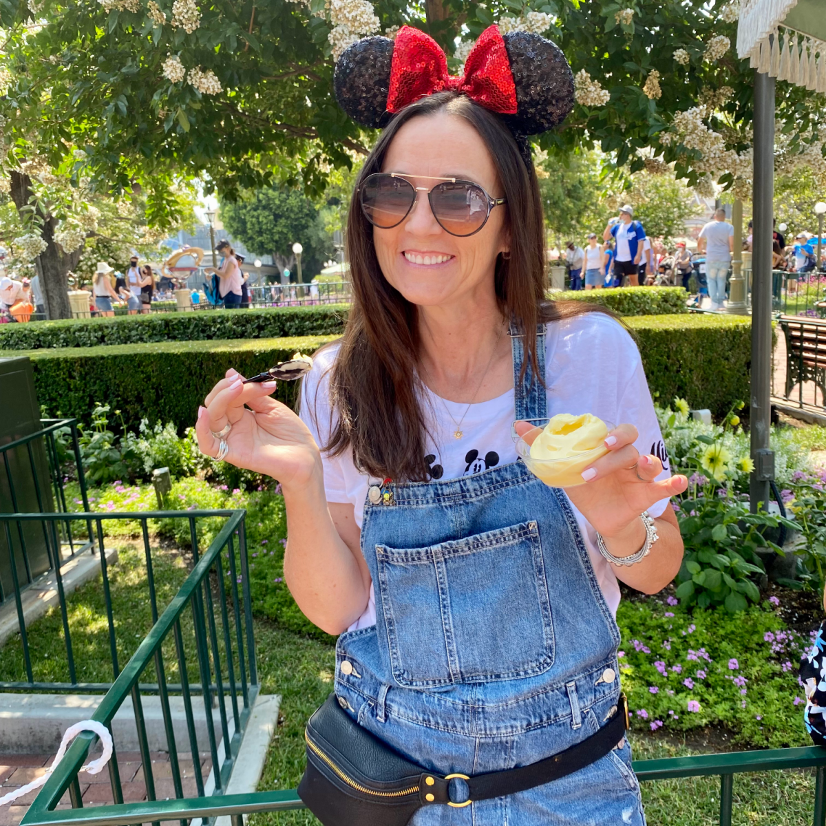 Woman in overalls with Mickey Mouse ears on eating Dole Whip at Disneyland